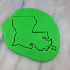Könnte beinhalten: Grüner Plastik-Ausstecher in Form des Bundesstaates Louisiana. Der Ausstecher liegt auf einer weißen Marmorfläche.