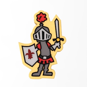 Puede incluir: Un cortador de galletas de caballero de dibujos animados con un casco rojo y blanco, una capa roja, una espada y un escudo con una flor de lis. El cortador de galletas es amarillo y tiene un fondo blanco.