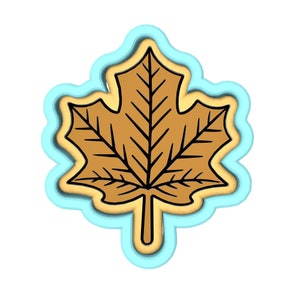 May include: A brown maple leaf cookie cutter with a blue outline. The cookie cutter is shaped like a maple leaf with a detailed design.
