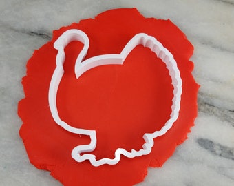 Puede incluir: Cortador de galletas de pavo de plástico blanco sobre una superficie de fondant roja.
