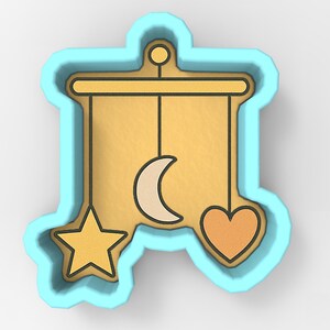 Könnte beinhalten: Ausstecher in Form eines Babymobils. Das Mobile hat einen goldfarbenen Hintergrund mit einem Stern, einem Mond und einem Herzen, die daran hängen. Der Ausstecher ist hellblau umrandet.