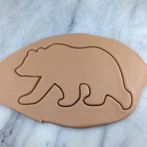 Könnte beinhalten: Ein brauner Plätzchenteig mit einem hineingedrückten Ausstecher in Form eines Bären.