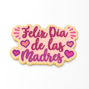 May include: A pink and yellow cookie with the text "Feliz Dia de las Madres" in pink and purple lettering. There are four pink hearts around the text.