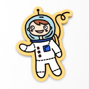May include: A yellow cartoon astronaut wearing a white spacesuit, blue helmet, and red details. The astronaut is smiling and waving.