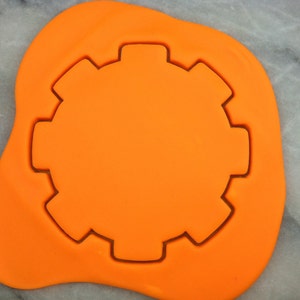 May include: Orange fondant with a gear-shaped cookie cutter pressed into it.