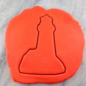 May include: A red cookie dough sheet with a lighthouse cookie cutter pressed into it.