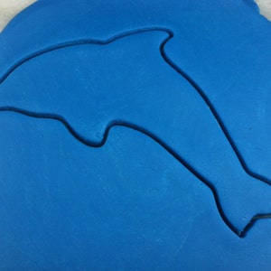 May include: A blue fondant cookie dough sheet with a dolphin-shaped cutout.