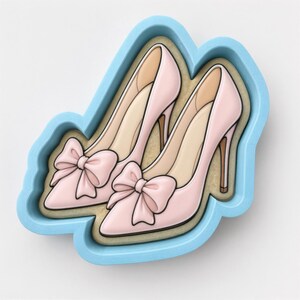 May include: A light blue plastic cookie cutter shaped like a pair of high-heeled shoes. Inside the cutter is a biscuit decorated with light pink icing, featuring a pointed toe, a tall stiletto heel, and a prominent bow on the front of each shoe.