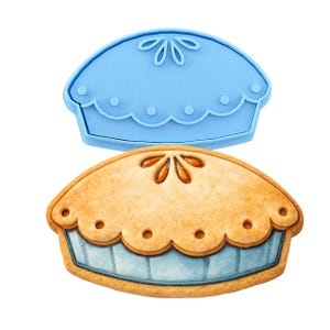 May include: A light blue pie-shaped cookie cutter next to a decorated pie. The pie has a golden-brown crust with a scalloped edge and a light blue base. The cookie cutter is made of plastic.