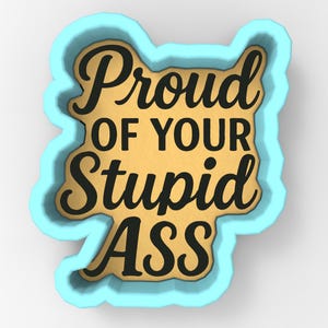 Puede incluir: Cortador de galletas azul claro y dorado con la frase "Proud of Your Stupid ASS" en negro. El texto está centrado dentro de la forma dorada.
