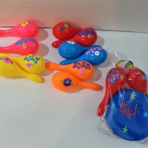 May include: A set of colourful maracas with names written on them, including "Eden", "Lily", and "Eli". There is also a blue tambourine with stars and the name "Eli" written on it.