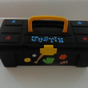 May include: Black plastic toolbox with a yellow handle and a baseball theme. The toolbox has a nameplate that says "Justin" in blue letters. The toolbox has a baseball bat, baseball, glove, and football on the front.