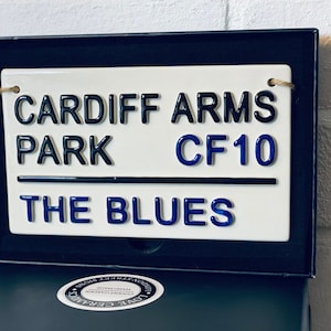 May include: White ceramic sign with black and blue lettering. The sign reads "Cardiff Arms Park CF10 The Blues".