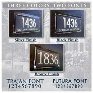 May include: Three house number signs with different finishes: silver, black, and bronze. The signs feature the numbers 1436 and 1836. The text "SQUAW VALLEY DR." is on the top of the signs. The signs are displayed against a background of greenery. The text "TRAJAN FONT" and "FUTURA FONT" are displayed below the signs, along with the numbers 1234567890.