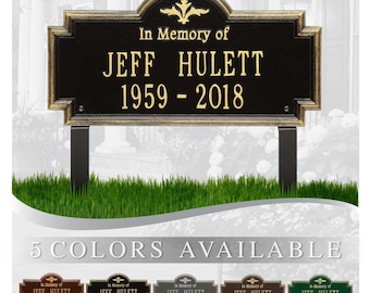 May include: A black metal memorial sign with gold accents and the text "In Memory of JEFF HULETT 1959-2018". The sign is on a wooden post and is surrounded by green grass. Five different color options for the sign are shown below.