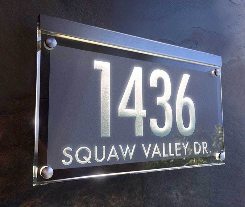 May include: A modern house number sign with a silver frame and clear glass. The number 1436 is displayed in white on a dark gray background. The street name "SQUAW VALLEY DR." is also displayed in white.