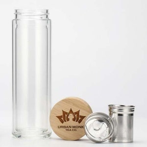 May include: A clear glass tea bottle with a bamboo lid and a stainless steel infuser. The lid has a brown logo that says "Urban Monk Tea Co."