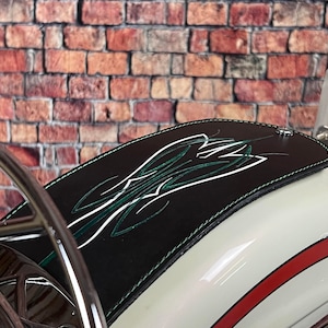 K&ouml;nnte beinhalten: Schwarzer Leder-Kotfl&uuml;gel f&uuml;r Motorr&auml;der mit gr&uuml;nen und wei&szlig;en Zierstreifen. Der Kotfl&uuml;gel ist an einem wei&szlig;en Motorrad mit einem roten Streifen befestigt.