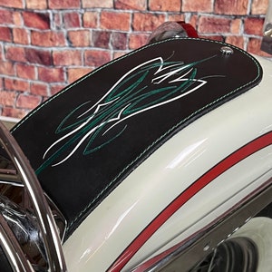 K&ouml;nnte beinhalten: Ein wei&szlig;er Motorradkotfl&uuml;gel mit einer schwarzen Lederabdeckung. Die Abdeckung hat ein gr&uuml;n-wei&szlig;es Pinstripe-Design. Der Kotfl&uuml;gel hat einen roten Streifen am Rand.