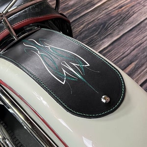 K&ouml;nnte beinhalten: Schwarzer Leder-Motorradkotfl&uuml;gel mit einem gr&uuml;nen und wei&szlig;en Pinselstrich-Design. Der Kotfl&uuml;gel ist an einem wei&szlig;en Motorrad mit Chromzierleisten befestigt.