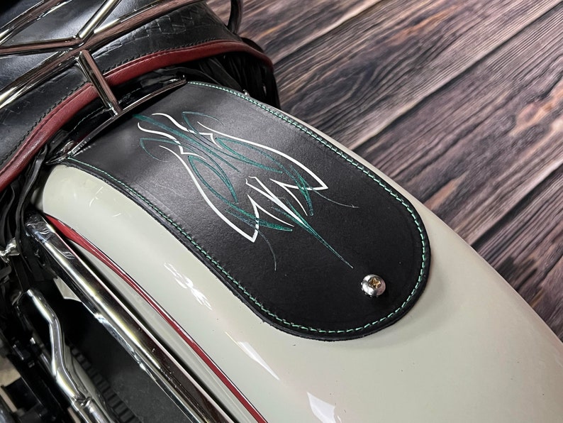 K&ouml;nnte beinhalten: Schwarzer Leder-Motorradkotfl&uuml;gel mit einem gr&uuml;nen und wei&szlig;en Pinselstrich-Design. Der Kotfl&uuml;gel ist an einem wei&szlig;en Motorrad mit Chromzierleisten befestigt.