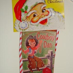 May include: Vintage Christmas stocking with a Santa Claus face and the words "Merry Christmas" on top. The stocking features a cowboy-themed design with a cowboy riding a bucking bronco. The stocking is filled with marbles and an orange.
