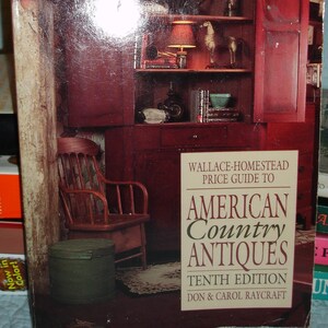 May include: A book cover for "Wallace-Homestead Price Guide to American Country Antiques, Tenth Edition." The cover features a red cabinet with open doors, a wooden chair, and a green container. The text "1991 Prices" is visible.