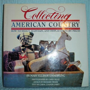 May include: A book cover titled "Collecting American Country" with a red and white banner. The cover features a wooden box filled with country-style items, including a teddy bear, a rocking horse, and other decorative pieces.
