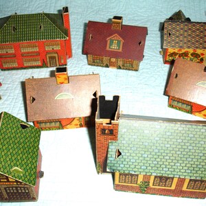 Puede incluir: Una colecci&oacute;n de casas de cart&oacute;n en miniatura de colores, con varios estilos de tejados y revestimientos de ladrillo o madera. Las casas presentan detalles como chimeneas, ventanas y puertas, lo que sugiere un tema de pueblo o ciudad.