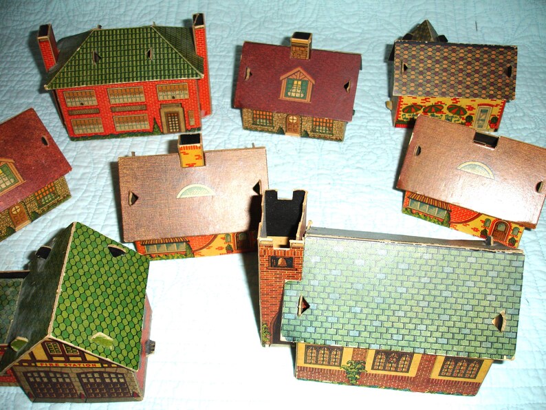 Puede incluir: Una colecci&oacute;n de casas de cart&oacute;n en miniatura de colores, con varios estilos de tejados y revestimientos de ladrillo o madera. Las casas presentan detalles como chimeneas, ventanas y puertas, lo que sugiere un tema de pueblo o ciudad.