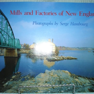 May include: A book cover titled "Mills and Factories of New England" with a photograph by Serge Hambourg. The image shows a green bridge over a river, with a factory and water reflections. The sky is blue.