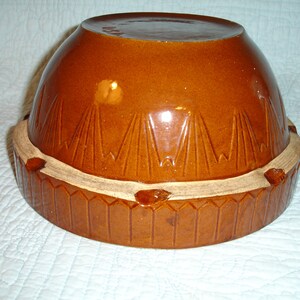 May include: A brown ceramic mixing bowl with a matching base. The bowl has a rounded shape with a glossy finish and a decorative pattern of vertical lines. The base has a geometric design and a lighter-colored rim.