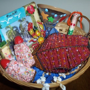 May include: A wicker basket filled with beach-themed items. Includes a beaded red clutch, a framed picture with palm trees, a martini glass with star accents, and decorative items. The basket is lined with blue tissue paper.
