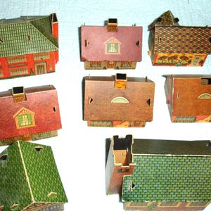 Puede incluir: Una colecci&oacute;n de casas de papel vintage en varios colores y dise&ntilde;os. Las casas presentan tejados rojos, verdes y marrones, con fachadas y chimeneas detalladas. Algunas tienen ventanas y patrones decorativos.