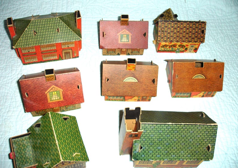 Puede incluir: Una colecci&oacute;n de casas de papel vintage en varios colores y dise&ntilde;os. Las casas presentan tejados rojos, verdes y marrones, con fachadas y chimeneas detalladas. Algunas tienen ventanas y patrones decorativos.