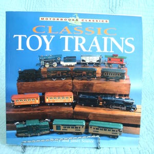 May include: A book titled "Classic Toy Trains" with a blue cover. The cover features various toy train cars and locomotives displayed on wooden blocks. The text "MOTORBOOKS CLASSICS" is at the top.