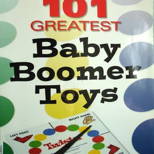 May include: A book cover titled "Warman's 101 Greatest Baby Boomer Toys" with a Twister game board. The cover features large red and black text on a white background with colorful circles. A black spinner is on the Twister board.