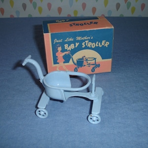 May include: A vintage baby stroller toy in light blue, with a matching box. The box is orange and blue, with the words "Baby Stroller" and an illustration of a person pushing a stroller. The toy has four wheels.