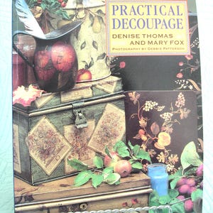 May include: A book cover titled "Practical Decoupage" by Denise Thomas and Mary Fox. The cover features a still life with a decorative chest, apples, and a pitcher. The color palette includes greens, browns, and reds.
