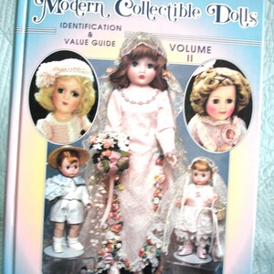 May include: A book titled "Modern Collectible Dolls" with a light blue cover. The cover features images of vintage dolls, including a bride doll and other dolls in various outfits. The book is a volume II identification and value guide.