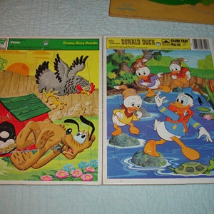 Puede incluir: Dos rompecabezas vintage de marco y bandeja con personajes de Disney. Un rompecabezas representa a Pluto, una gallina y una caseta para perros. El otro rompecabezas muestra a Donald Duck y sus sobrinos. Los rompecabezas son de cartón y tienen un diseño colorido.