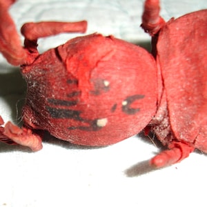 May include: A handmade red insect-like sculpture with black markings and white dots. The sculpture has multiple appendages and is lying on a white surface. The overall theme is a whimsical, handcrafted art piece.