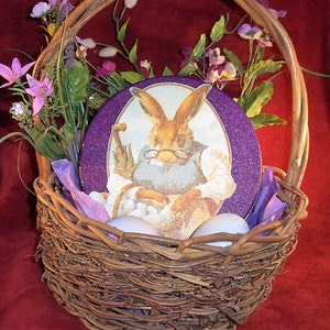 May include: A woven wicker Easter basket with a handle, filled with purple tissue paper, faux flowers, and a decorative oval featuring a rabbit with glasses. The basket also contains white eggs.
