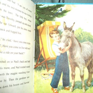 May include: Vintage children's book illustration featuring a young boy hugging a donkey. The boy wears blue overalls and a white shirt. A yellow and white striped beach chair and a bird are in the background. The book is open.