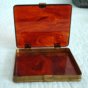 May include: Open vintage rectangular box with a hinged lid. The box has a brass frame and a tortoiseshell-patterned interior. The lid is open, revealing the interior. The box is empty.