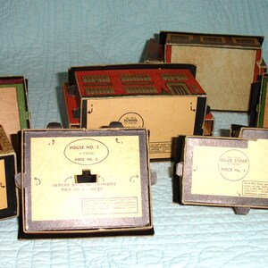 Puede incluir: Colecci&oacute;n de edificios de juguetes de cart&oacute;n vintage, incluyendo una estaci&oacute;n de bomberos y casas. Los edificios tienen detalles en beige, rojo y verde. Las cajas tienen texto que dice "Fire Station Piece No. 1" y "House No. 2".
