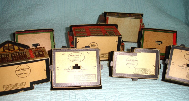 Puede incluir: Colecci&oacute;n de edificios de juguetes de cart&oacute;n vintage, incluyendo una estaci&oacute;n de bomberos y casas. Los edificios tienen detalles en beige, rojo y verde. Las cajas tienen texto que dice "Fire Station Piece No. 1" y "House No. 2".