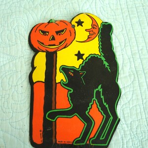 May include: Vintage Halloween decoration featuring a jack-o'-lantern, crescent moon with a face, and a black cat with green outlines. The background is yellow and orange. The cat is arched with its mouth open. The decoration is made of cardboard.
