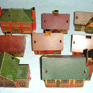 Puede incluir: Una colecci&oacute;n de casas de papel vintage con fachadas detalladas y tejados a dos aguas. Las casas presentan varios colores, incluyendo rojo, verde y marr&oacute;n, con intrincados dise&ntilde;os de ventanas y puertas. La disposici&oacute;n muestra la variedad de estilos arquitect&oacute;nicos.