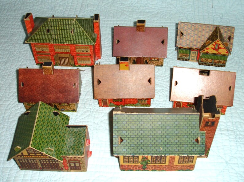 Puede incluir: Una colecci&oacute;n de casas de papel vintage con fachadas detalladas y tejados a dos aguas. Las casas presentan varios colores, incluyendo rojo, verde y marr&oacute;n, con intrincados dise&ntilde;os de ventanas y puertas. La disposici&oacute;n muestra la variedad de estilos arquitect&oacute;nicos.